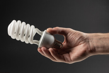 Energy saving concept. Male hand holding light bulb on dark background