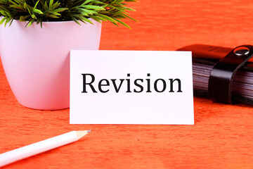 Revision word it is written on a white business card next to a business card holder, pencil and plants in a white pot