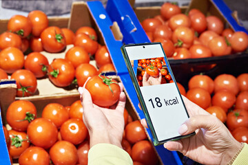 Checking calories on tomato vegetable in store with smartphone