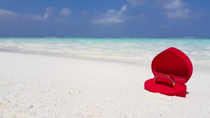 Closeup of a wedding ring in the red heart-shaped box on the sand of a tropical beach