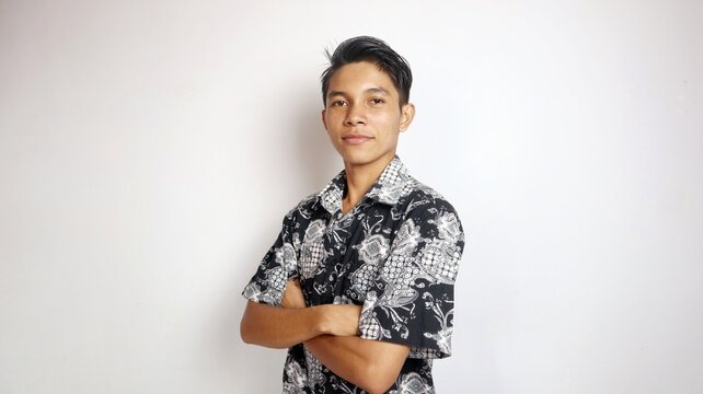 smiling young handsome Asian man wearing batik shirt posing with crossed arms