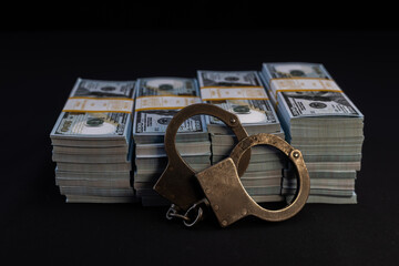 Handcuffs against a background of packs of dollars with bank tape on a black background. Money and...