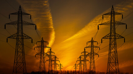 Two files of transmission towers against an orange sunset sky