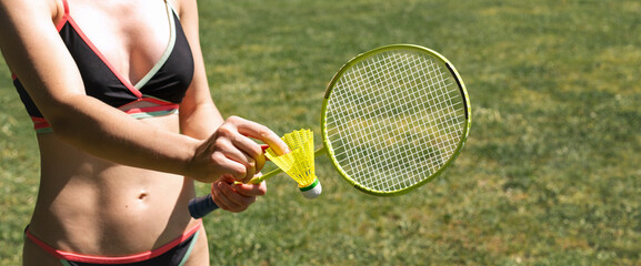 Attractive sporty woman in two-piece swimsuit playing badminton at resort. Shuttlecock and badminton racket in females hands.