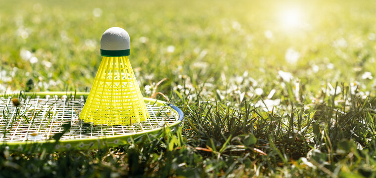 Yellow shuttlecock and badminton racket on the green grass of lawn.