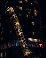 Illuminated tower crane by a high building apartments at night