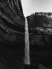 Vertical grayscale shot of a beautiful waterfall streaming down from the rocky cliff