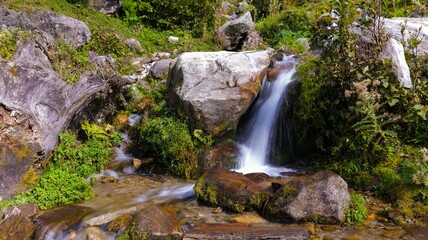 Small waterfall flowing over the rocks and stones with vegetation nearby