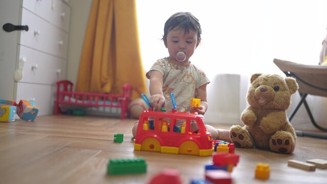 baby plays with toy bear a toy bus and puts wooden sticks in the hatch. development of fine motor skills concept. baby learns to put sticks toys into lifestyle a bus car indoors in kindergarten