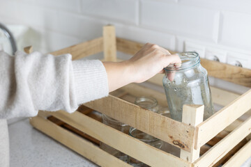 Glass recycling. A woman's hand puts a glass jar into a drawer on the kitchen table. The wooden box...