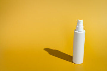 Blank white spray bottle on yellow background in direct sunlight. Summer skin protection mockup...