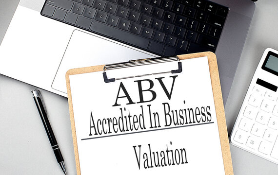 ABV -ACCREDITED IN BUSINESS VALUATION word on clipboard on laptop with calculator and pen