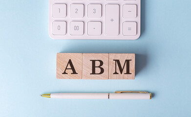 ABM word on wooden block with pen and calculator on blue background
