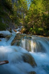 Long exposure shot of a cascade river surrounded by green trees on a sunny day