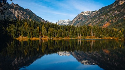 Trees of the dense forest and mountains reflected in the waters of a calm lake in Washington