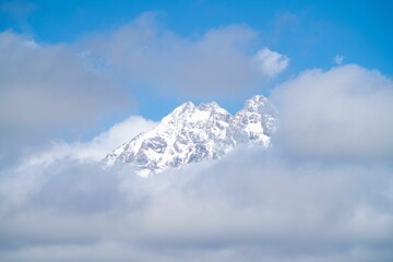 Scenic view of a mountain peak covered in snow seen behind the clouds