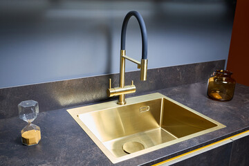 Luxurious interior square golden brass sink and faucet double tap mixer in contemporary modern design with stone marble stoneware countertop black and gold kitchen with sandwatch and glass pot
