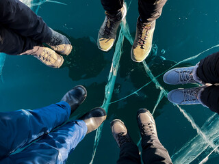 Fragile thin brittle ice underfoot. Male and female feet on ice. Cracks on ice background. Ice of Lake Baikal. - obrazy, fototapety, plakaty