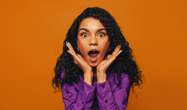 Surprised woman with curly hair on vibrant orange background