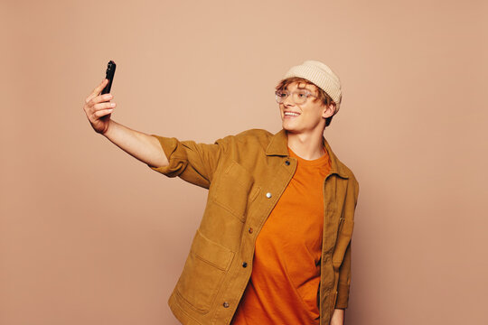Happy man taking a vibrant selfie with a phone in a peach background