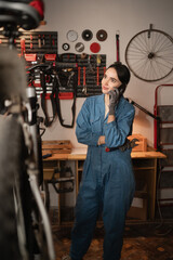 woman mechanic talking on phone, asking for help on repairing damaged bike, standing in garage or workshop. telephone call with bicycle engineer