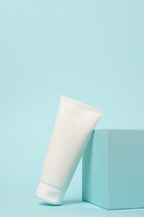 White cosmetic tube on the podium on blue background, copy space