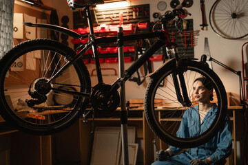 Female worker crouching and repairing bicycle. Bike workshop interior.