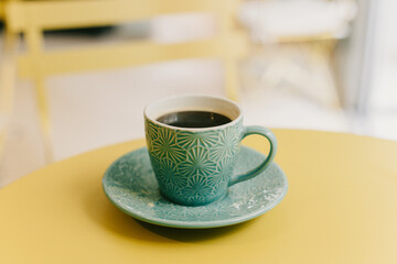 Cup of black coffee in turquoise ceramic cup on a yellow table in a cafe.