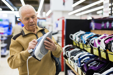 Elderly man choosing iron in showroom of electrical appliance store