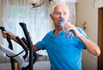 Senior man using elliptical trainer and drinking water