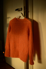 knitted sweater in orange color, on a hanger on a door
