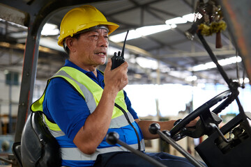 senior worker using walkie talkie and holding steering wheel on forklift truck in the factory
