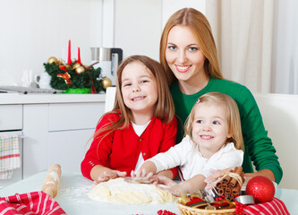 Two adorable girls with mother baking Christmas cookies in the kitchen