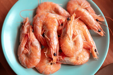 Shrimps in a blue plate on a wooden table, top view
