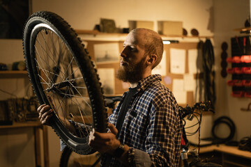Red Haired bearded male worker holding and repairing bicycle wheel while standing in bicycle...