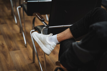 A person in white sneakers sits on a chair on hardwood flooring