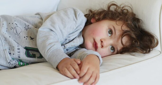 Young boy resting on a white sofa, looking unwell and tired