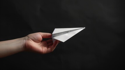 On a black background, a hand throws a white paper plane.