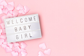 Welcome baby girl. Lightbox with letters and confetti in a heart shape on a pink pastel background.