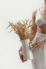 Naklejka premium Young woman holding ceramic pitcher with wheat spikes bouquet, Celiac Disease And Gluten Intolerance