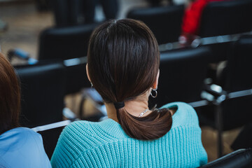 Woman in blue sweater seated among chairs at event