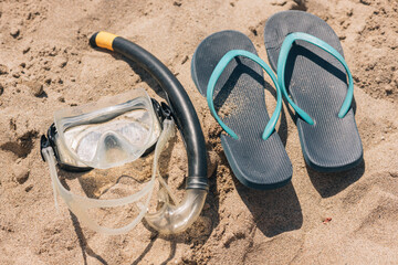A pair of Blue flip flops and a snorkeling mask are on the beach