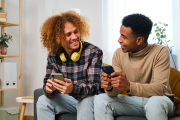 Young male flat mates smiling and using their smartphones together at shared apartment.