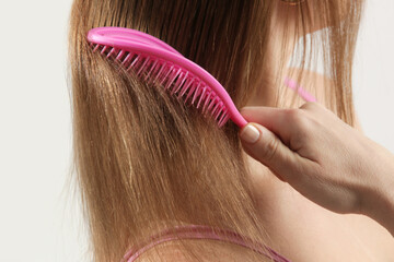 Hair care. Close up view of brunette woman combing her dry damaged hair with plastic detangling...