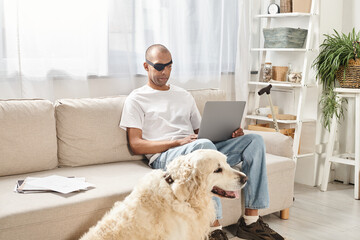 A man with myasthenia gravis syndrome works on a laptop while a loyal Labrador dog keeps him...