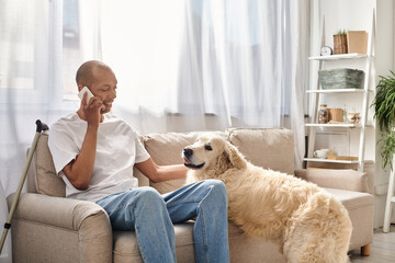 An African American man, disabled with myasthenia gravis, sits on a couch talking on a cell phone...