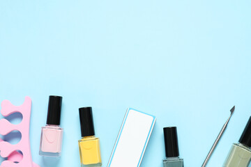 Nail polishes, toe separators, buffer and cuticle pusher on light blue background, flat lay. Space...