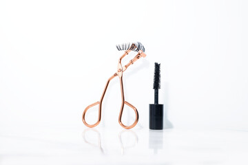 An arrange of fake eyelashes, tweezer and a small black mascara with in a white background