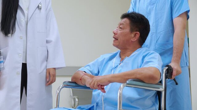 An elderly young asian man patient sitting a wheelchair being attended to by medical staff talking and discussing with doctor in a clinic or hospital, senior patient receiving care for physician.