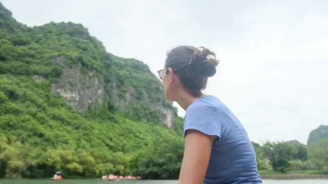 Woman with her back on a boat in Vietnam in Tam Coc exploring the wonders of the area and nature. Solo woman travel adventures in Southeast Asia, discovering new cultures and adventures.